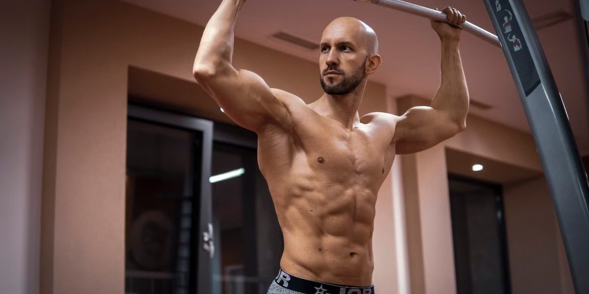 A bald, muscular man performing exercise on gym equipment indoors.
